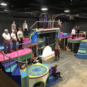 Cast rehearsing on a colorful set of twisting stairs and balconies.